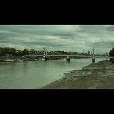 a river with boats on it and a bridge in the distance, under a cloudy sky