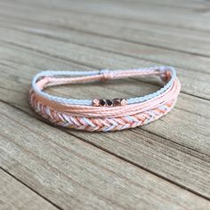 the pink and white braid bracelet is on top of a wooden table with two small beads