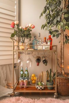 a bar cart filled with bottles and glasses on top of a table next to a potted plant