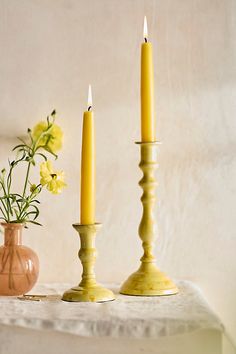 two yellow candles sitting on top of a table next to vases filled with flowers