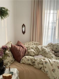 an unmade bed in a bedroom with flowers on the table and curtains behind it