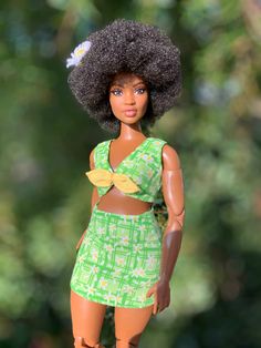 a doll with an afro is standing on a wooden platform in front of some trees