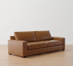 a brown leather couch sitting on top of a hard wood floor next to a white wall