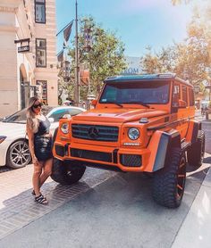 a woman standing next to an orange mercedes g class