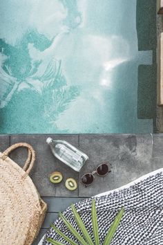 an empty bottle, straw bag and sunglasses on the ground next to a pool