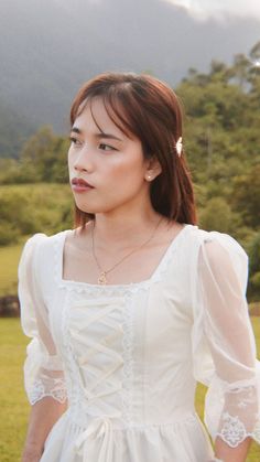 a young woman in a white dress standing on a lush green field with mountains in the background