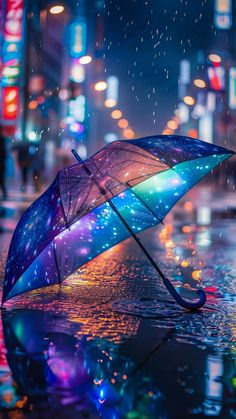 an open umbrella sitting on the side of a wet street at night with lights in the background