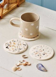 coffee cup and coasters sitting on a table with seashells scattered around them