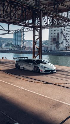 a white sports car parked under an overpass next to the water with buildings in the background