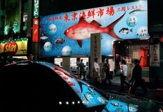 people are walking on the street at night in front of a building with an advertisement for fish