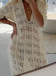 a woman in a white crochet dress taking a selfie with her cell phone