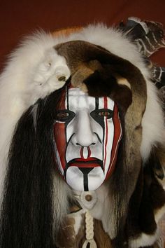 a man with long hair wearing a white and red mask on his face is standing in front of a brown wall