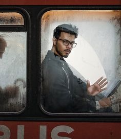 a man in glasses looking out the window of a train with his hand on an open book