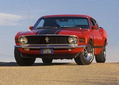 an old red car with black stripes parked on the side of the road in front of a tree