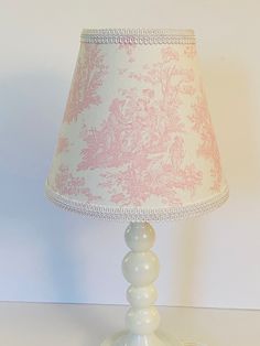 a lamp that is sitting on top of a white table with a pink and white lampshade