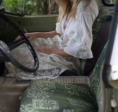 a woman sitting in the back seat of a green car with white lace on it