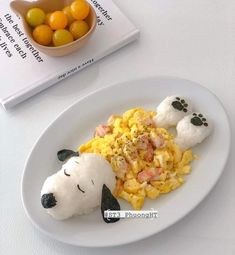a white plate topped with food next to a bowl of oranges and a book