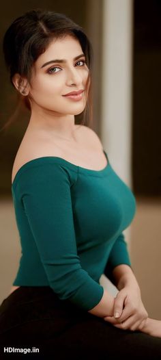 an attractive young woman in green top posing for the camera with her hands on her hips