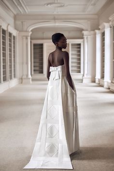 a woman in a white dress is standing in an empty room with columns and windows