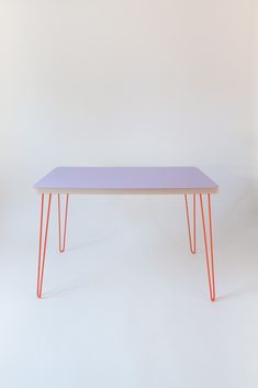 a purple table with orange legs on a white background in front of a pink wall