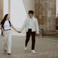 a man and woman holding hands walking down the street