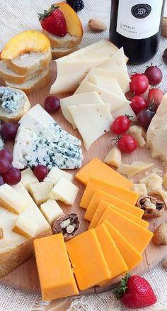 various cheeses, fruits and nuts are arranged on a cutting board next to a bottle of wine