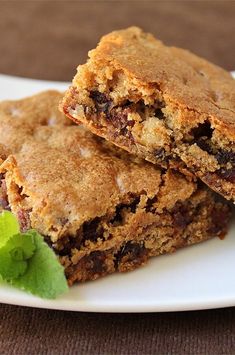 two pieces of chocolate chip cookie sitting on top of a white plate next to a green leaf