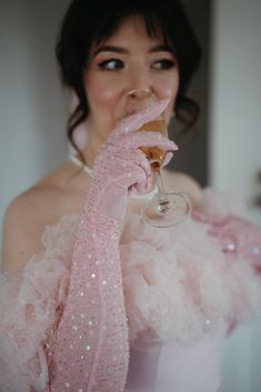 a woman in a pink dress holding a wine glass up to her mouth and wearing a pink scarf around her neck