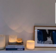 two lit candles sitting on top of a white shelf next to a book and framed photograph