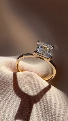 a diamond ring sitting on top of a white cloth next to the shadow of a person's hand