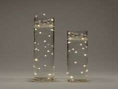 two glass vases with lights in them sitting side by side on a gray surface