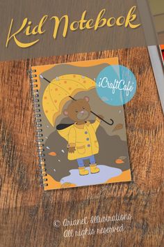 a spiral notebook with a cartoon bear holding an umbrella on top of a wooden table