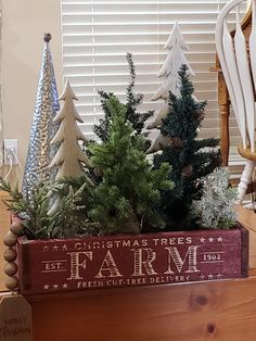 a wooden box filled with christmas trees sitting on top of a table next to a window