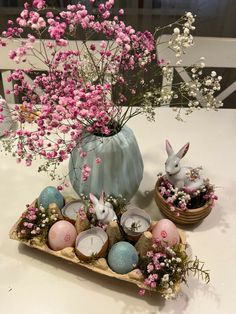 an arrangement of flowers, candles and bunny figurines on a white table top