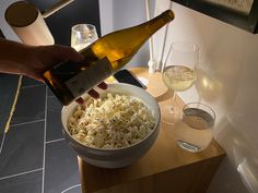 a person pouring wine into a bowl full of popcorn