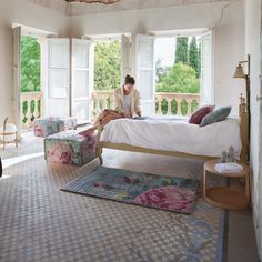 a woman sitting on top of a bed in a bedroom next to two chairs and a table