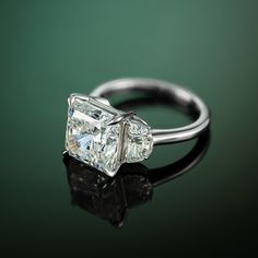 a three stone diamond ring sitting on top of a black surface with reflection in it