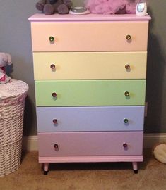 a pink teddy bear sitting on top of a multicolored dresser next to a basket