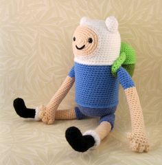 a crocheted stuffed animal with a blue shirt and black pants sitting on the ground