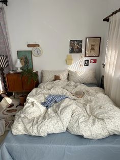 an unmade bed in a bedroom with pictures on the wall and curtains behind it