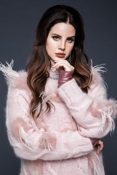 a woman with long hair wearing a pink sweater and feathered sleeves is posing for the camera