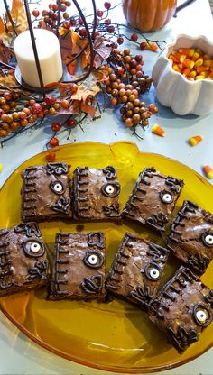 some brownies are on a yellow plate with candles and pumpkins in the background
