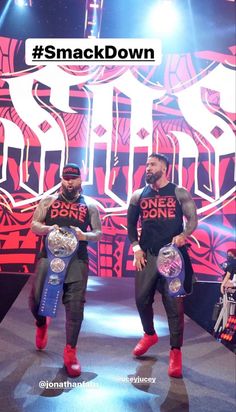 two men in black shirts and red boots holding up their wrestling belts while standing on a stage