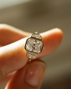 a woman's hand holding a ring with a white diamond in the middle,