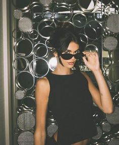 a woman wearing sunglasses is standing in front of a wall with circles and round mirrors