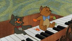 two cats are playing the piano with each other and one cat is holding something in his hand