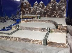 a model train set with mountains and snow on the ground in front of a blue wall