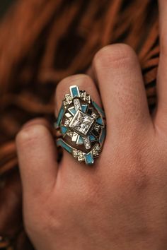 a close up of a person's hand wearing a ring with diamonds and blue stones