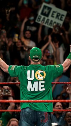 a man in a green shirt is holding his arms up and standing next to a wrestling ring