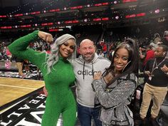 two women and a man posing for a photo in front of an audience at a basketball game